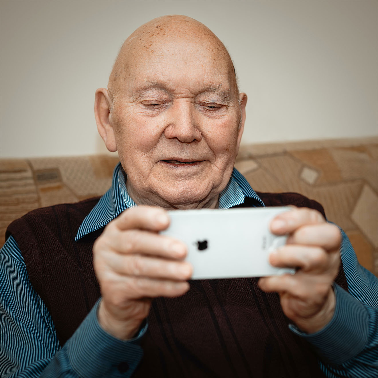 elderly man sat down playing on an iphone smilinh