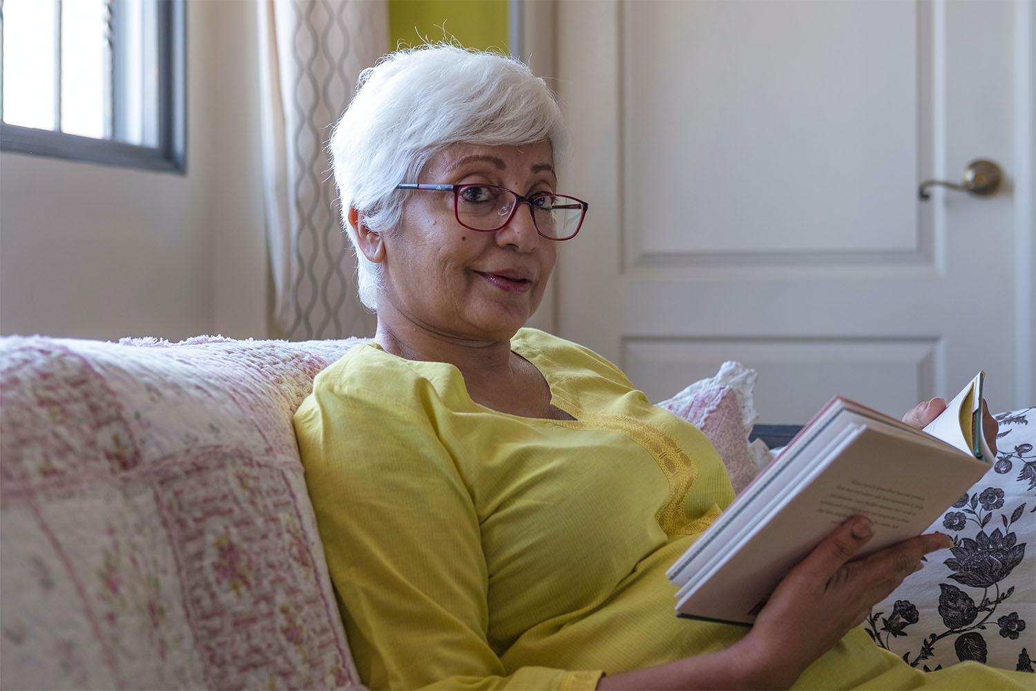 elderly woman sat down reading a book and smiling