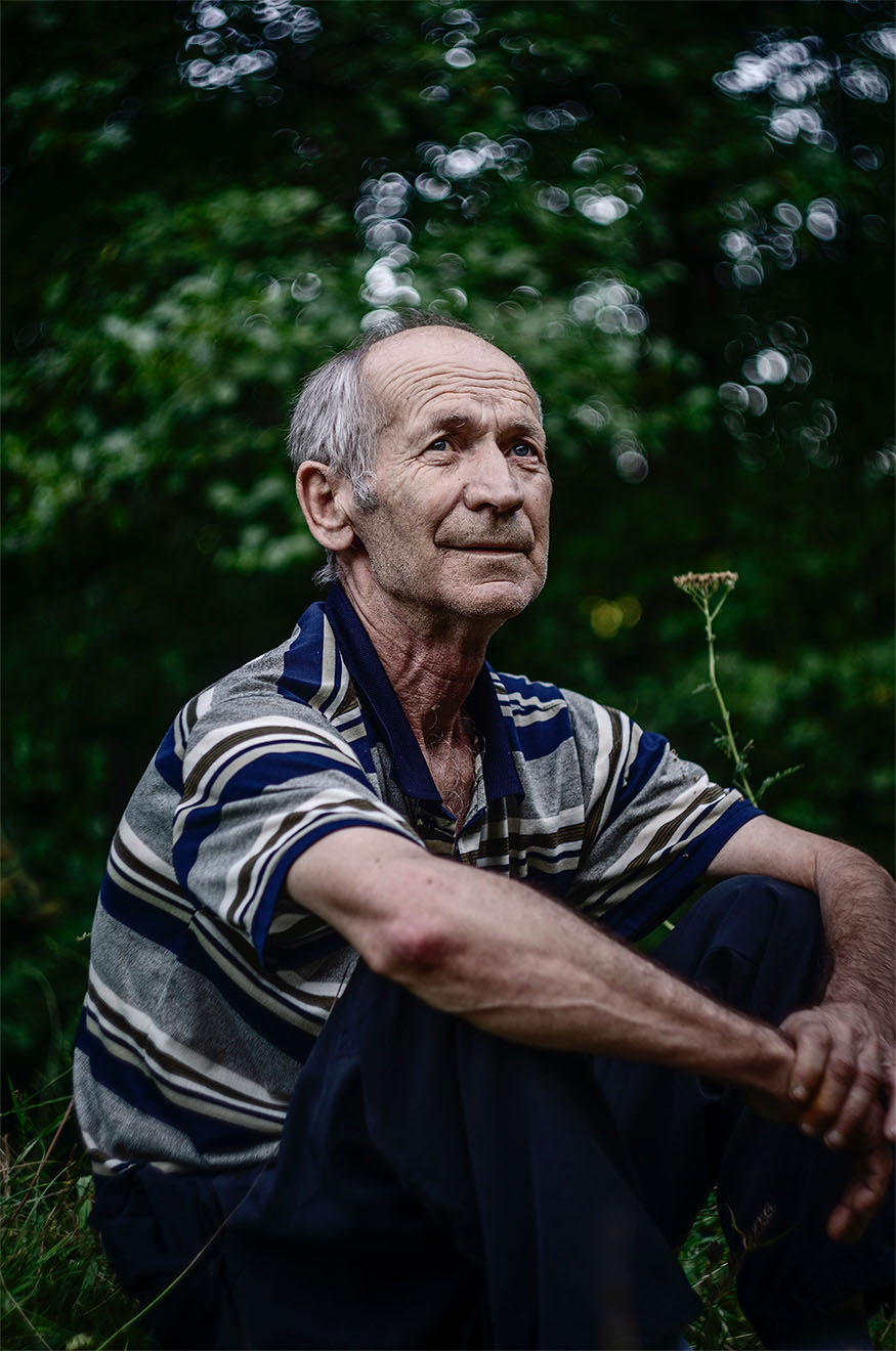 elderly man sat outside holding his legs looking into the distance