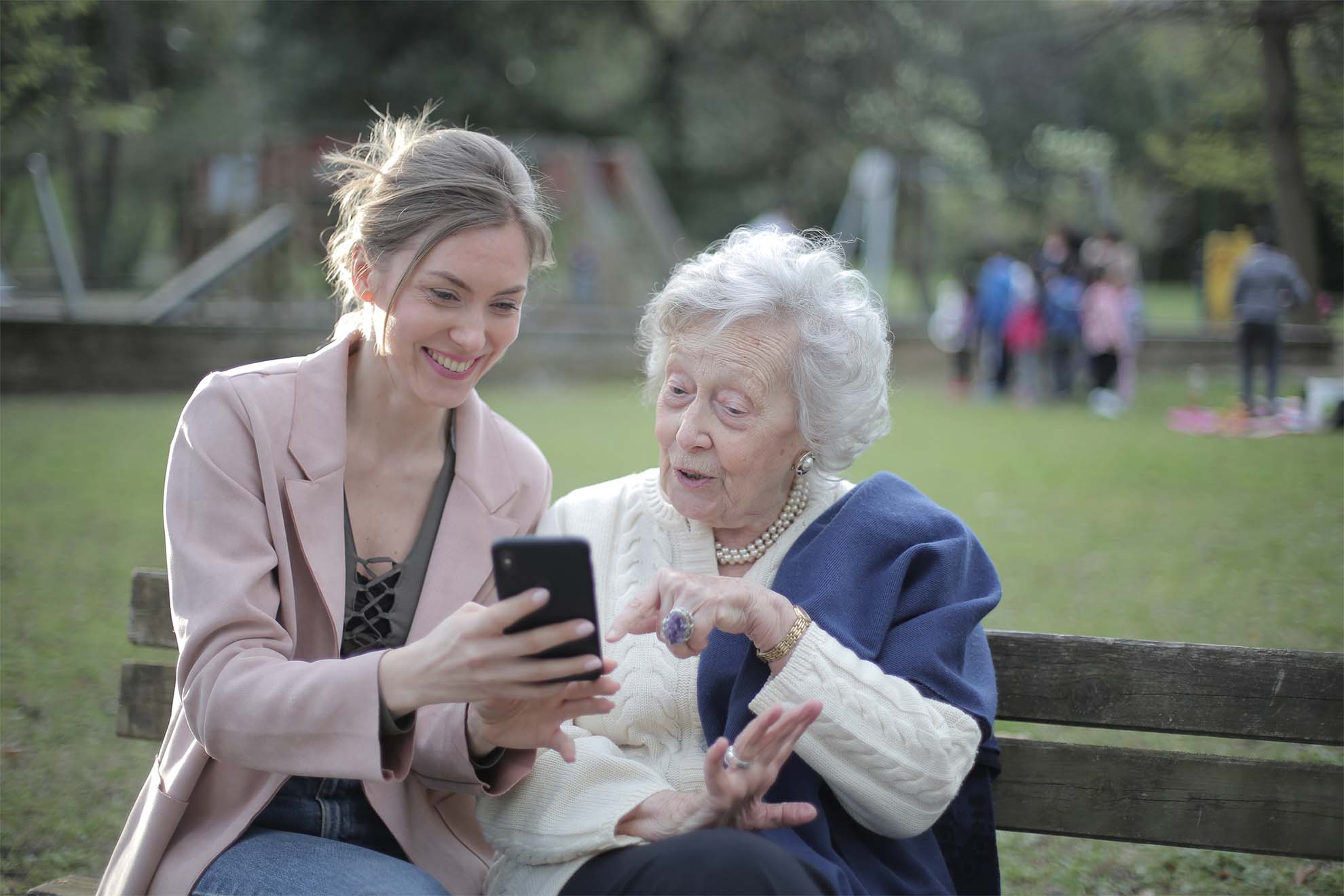 resident and a loved one sat on a bench in a park looking at something on a phone