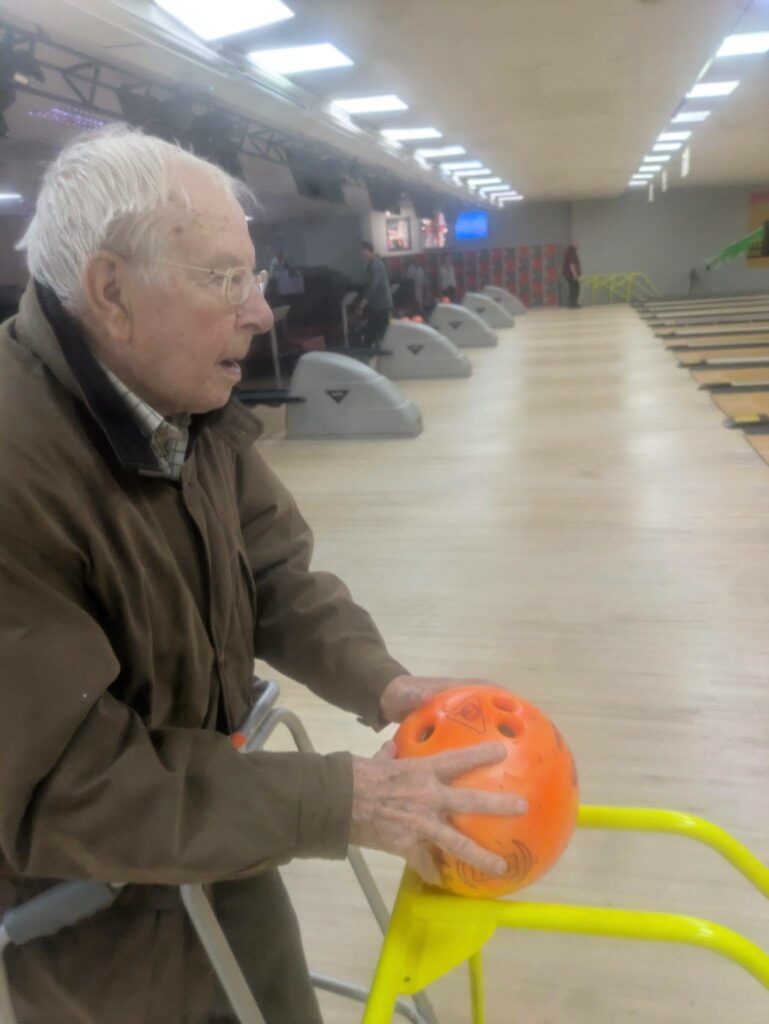 older man pushing a bowling ball down a ramp