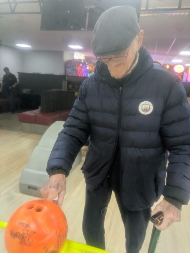 older man pushing a bowling ball down a ramp