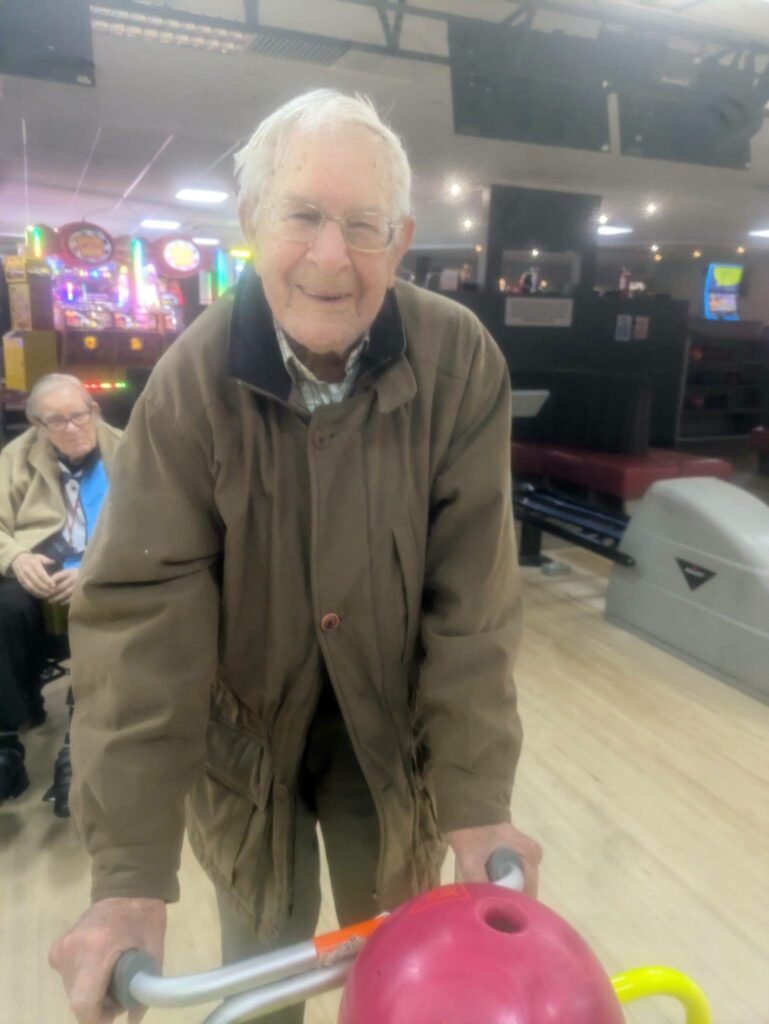 older man pushing a bowling ball down a ramp